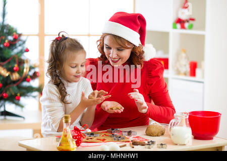 Madre e figlia la cottura biscotti di Natale a decorate albero. Mamma e Bambino cuocere i dolci di Natale. Famiglia con bambini festeggiano il Natale a casa. Foto Stock