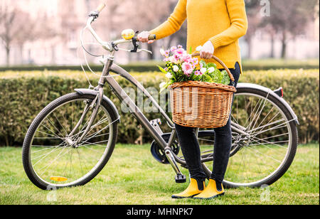 Giovane donna con la bicicletta in piedi fuori in primavera soleggiata. Foto Stock