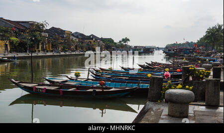 Barche con fiori di colore giallo e lanterne legato lungo il fiume nella vecchia città di Hoi An, Vietnam Foto Stock