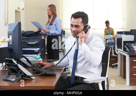 Imprenditore rendendo chiamata alla scrivania in ufficio occupato Foto Stock