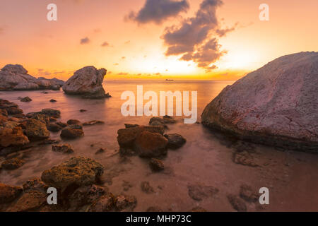 Vivace tramonto a rocciosa costa tropicale, petroliera all orizzonte, con esposizione lunga Foto Stock