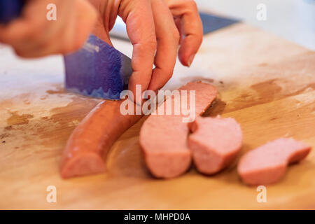 Le mani di salsiccia per affettare con lama blu su legno tagliere. Foto Stock