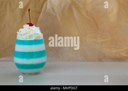 A strisce blu jella dessert in vetro con panna montata e rosso ciliegia candita sulla parte superiore Foto Stock