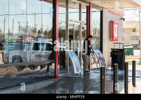 Un giovane uomo caucasico dipendente lavaggi di potenza il cemento al di fuori di un negozio QuickTrip di Wichita, Kansas, Stati Uniti d'America. Foto Stock