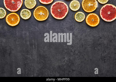 Piatto di laici agrumi modello di limone, arancia e pompelmo sulla pietra nera dello sfondo. Copia dello spazio sul fondo. Vista dall'alto. Foto Stock