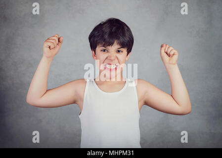 Kid che mostra i suoi muscoli su sfondo grigio Foto Stock