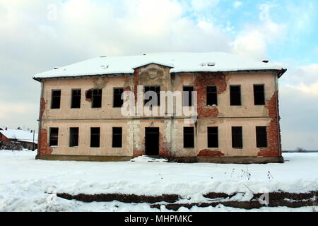 Abbandonato rovinato il vecchio edificio scolastico realizzato nell ultimo secolo senza finestre o porte e con il calo della facciata e i mattoni a vista coperto e surround Foto Stock