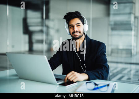 Giovane imprenditore lavora con computer portatile e le cuffie in ufficio, che simboleggiano il servizio di assistenza clienti Foto Stock