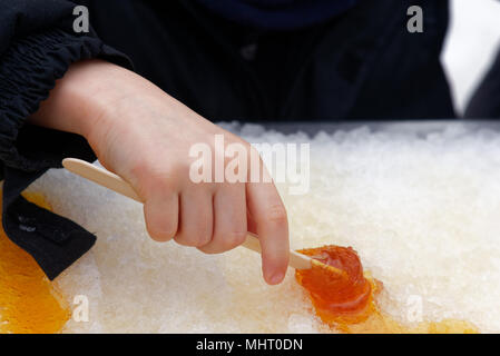 Close up di un giovane (5 anno di età del bambino la laminazione a mano lo sciroppo d'acero taffy su un bastone Foto Stock