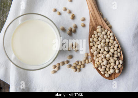I fagioli di soia in cucchiaio di legno con un bicchiere di latte di soia visualizzati direttamente dall'alto. Foto Stock