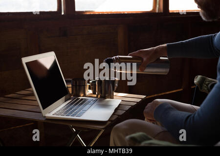 L'uomo versando il caffè dalla beuta da vuoto a scrivania Foto Stock