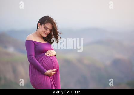 Brunette incinta giovane donna ritratto su sfondo al tramonto Foto Stock