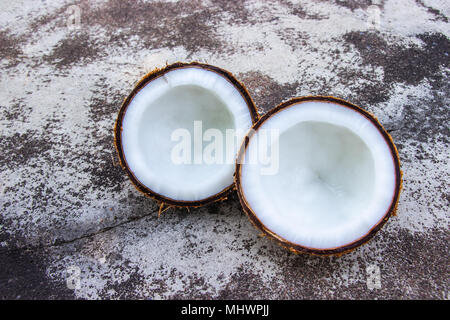 Mature mezza noce di cocco di taglio su una superficie khrap sfondo concreto. Foto Stock