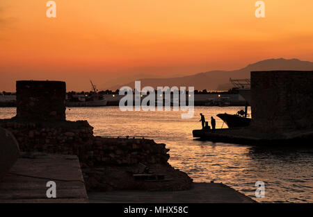 Persone di pesca al tramonto all'entrata del vecchio porto da pesca di Ierapetra town, prefettura di Lasithi, Creta, Grecia. Foto Stock