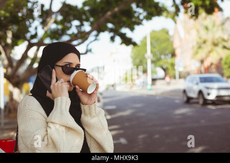 Il hijab donna parlando al telefono cellulare mentre avente un caffè a pavement cafe Foto Stock