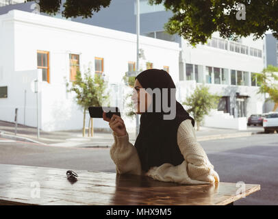 Urban hijab donna parlando al telefono mobile a pavement cafe Foto Stock