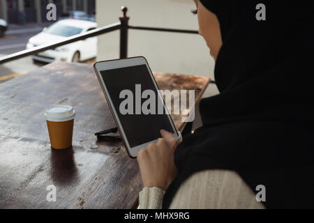 Il hijab donna utilizzando digitale compressa in cafe Foto Stock