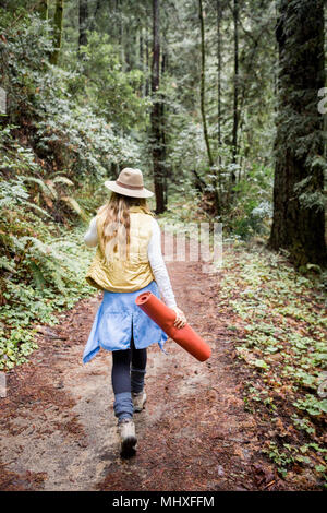 Giovane donna in trilby passeggiando nella foresta, vista posteriore Foto Stock