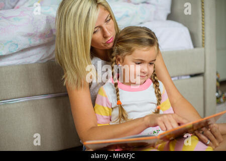 Metà donna adulta seduto sul piano di lettura con la figlia Foto Stock