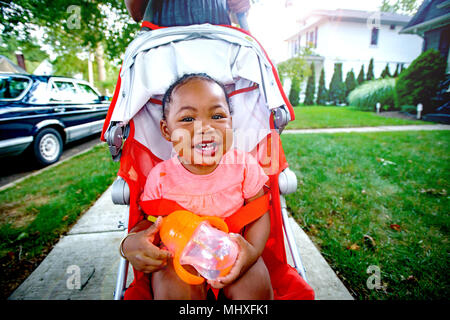 Happy Baby girl in passeggino sul marciapiede suburbane, ritratto Foto Stock