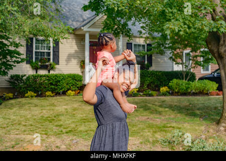 Metà donna adulta in giardino bambino portando figlia sulle spalle, ritratto Foto Stock