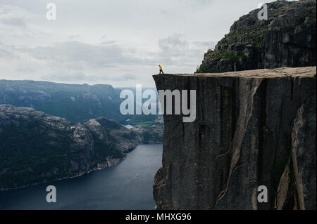 L'uomo traveler soddisfare l'alba seduto su Trolltunga scogliera rocciosa edge in Norvegia montagne Lifestyle Viaggi avventura vacanze estreme solo all'aperto al di sopra delle nuvole Foto Stock