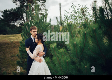 Appena sposata giovane teneramente bacio tra abeti Foto Stock