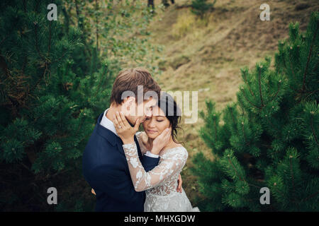 Appena sposata giovane teneramente bacio tra abeti Foto Stock