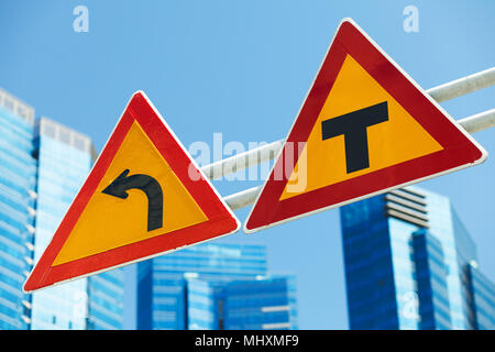 Pericoloso girare a sinistra e attraversare strade, avviso segni di traffico su blu dello skyline della città Foto Stock