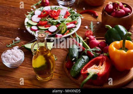 Fresco di ravanello rosso nella ciotola di legno tra le piastre con verdure, rucola e spezie in legno rustico sfondo, close-up, il fuoco selettivo e poco profonda dept Foto Stock