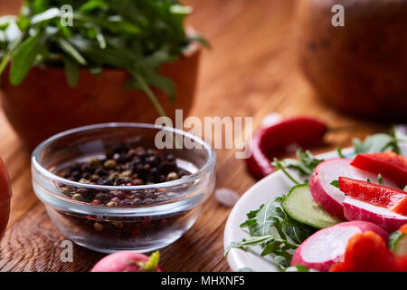 Fresco di ravanello rosso nella ciotola di legno tra le piastre con verdure, rucola e spezie in legno rustico sfondo, close-up, il fuoco selettivo e poco profonda dept Foto Stock