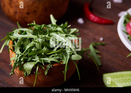 Fresco di ravanello rosso nella ciotola di legno tra le piastre con verdure, rucola e spezie in legno rustico sfondo, close-up, il fuoco selettivo e poco profonda dept Foto Stock