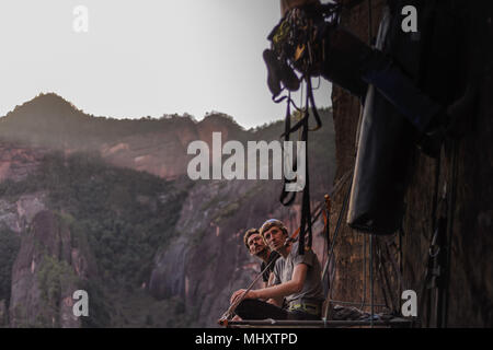 Due arrampicatori udienza del portaledge, guardando amico salire rock accanto a loro, la calcinazione, nella provincia dello Yunnan in Cina Foto Stock