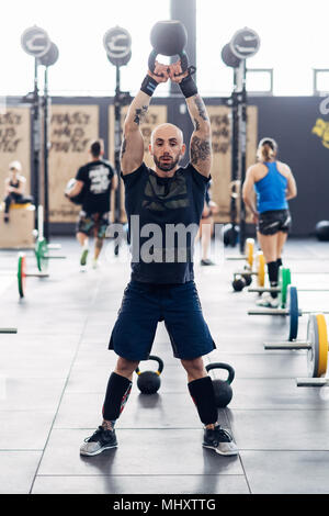 L'uomo il sollevamento pesi con bollitore campana in palestra Foto Stock