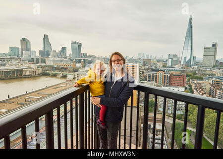 Donna e bambino figlia sul balcone con vista sullo skyline di Londra, ritratto Foto Stock