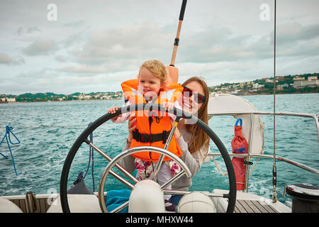 Donna yacht dello sterzo con il toddler figlia, ritratto, Devon, Regno Unito Foto Stock