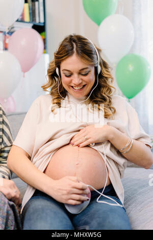 Donna incinta sul divano utilizzando prenatale di dispositivo di ascolto Foto Stock