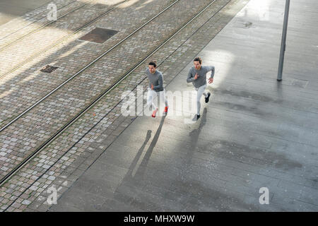 Giovani maschi adulti gemelli correndo insieme, che corre lungo il marciapiede, ad alto angolo di visione Foto Stock