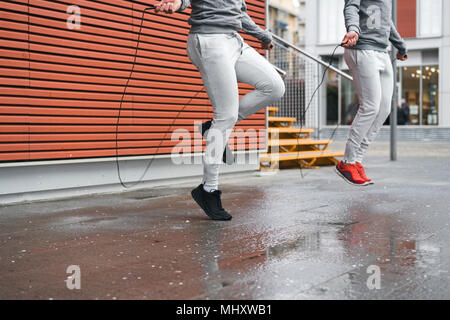 Maschio adulto gemelli formazione, saltando con funi sul marciapiede Foto Stock