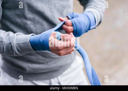 Giovane maschio boxer formazione all'aperto, fasciature mani con avvolgimenti a mano, metà sezione Foto Stock