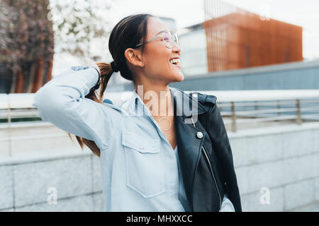 Ritratto di imprenditrice all'aperto, giacca di pelle poggiata sulla spalla, guardando lontano, sorridente Foto Stock