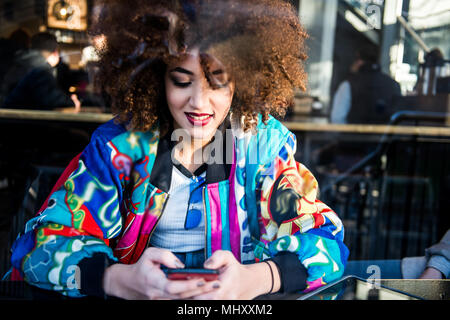 Giovane ragazza seduta nel bar, utilizza lo smartphone, vista attraverso la finestra, London, England, Regno Unito Foto Stock
