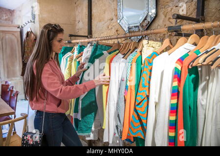 Giovane donna shopping, guardando i vestiti su rotaia in negozio Foto Stock