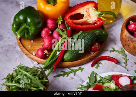 Creative verdura fresca insalata di rucola, cetriolo, pomodoro e raddish sulla piastra bianca su sfondo a trama, close-up, il fuoco selettivo. Mornin Foto Stock