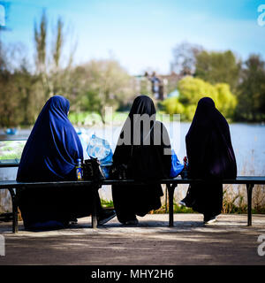 3 donne che indossano burkas sedersi sul bordo di un lago di mangiare il pranzo e di alimentazione della fauna selvatica Foto Stock