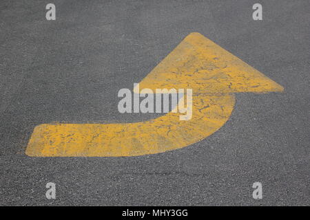 Traffico gialli freccia dipinta sul terreno di un parcheggio girando verso l'alto. Foto Stock