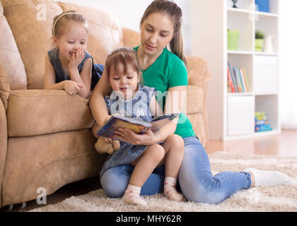 Madre e allegro figlie lettura libro in salotto Foto Stock