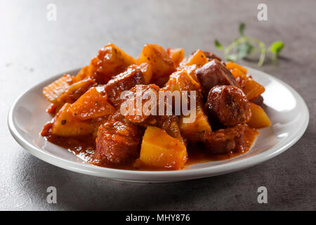 Patate spezzatino di maiale con le fette di salsiccia e salsa di pomodoro su una piastra bianca Foto Stock