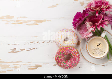 Tazza da caffè, ciambelle e gerbera fiori bianchi sul tavolo di legno. Vista da sopra con lo spazio per il testo Foto Stock