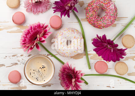 Tazza da caffè, ciambelle e gerbera fiori bianchi sul tavolo di legno. Vista superiore Foto Stock